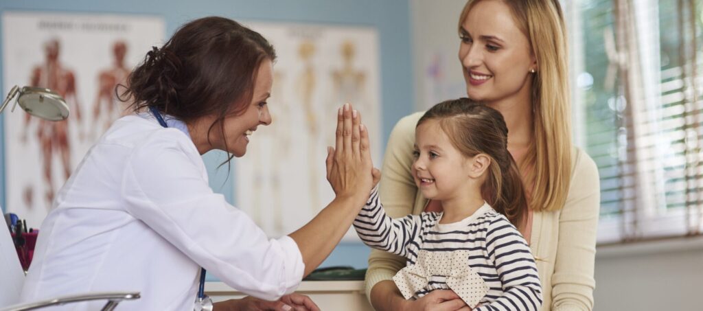 Mom and young daughter high fiving doctor at clinic.